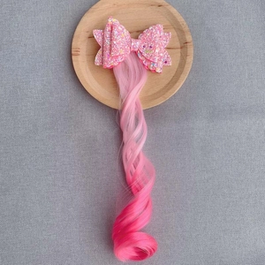Detail of pink gradient curly hairpiece with a large glittery sequin bow on a tray