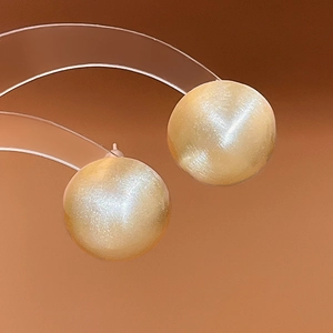 Close-up of golden geometric spherical stud earrings with subtle pearlescent shimmer