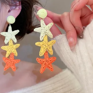 Handmade raffia star tassel earrings with yellow gradient pendant on model wearing white sweater