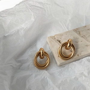 Detail of matte gold geometric interlocking hoop earrings on natural stone surface