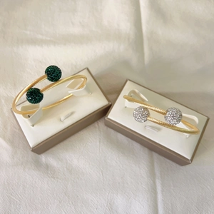 Détail d'un bracelet câble torsadé doré avec cristaux verts et blancs aux embouts