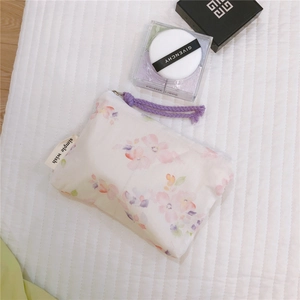 Detail of floral mini cotton pouch with purple cord zipper and brand label on soft padding