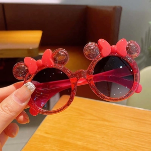Close-up of glittery red kids sunglasses with cartoon bow and round ear frames