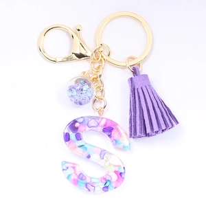 Detail of crystal resin letter S keychain with colorful stones, purple tassel and gold ring