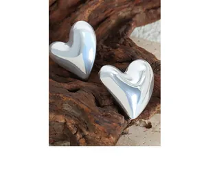 Macro detail of high-polish silver heart earrings resting on natural wood background