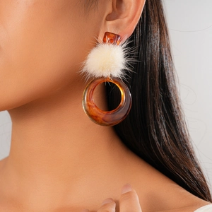 Detailed view of winter earrings with white pom-pom and amber resin hollow circle on model