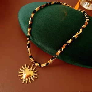 Dettaglio del cordino in tessuto leopardato e ciondolo cuore sole dorato su velluto