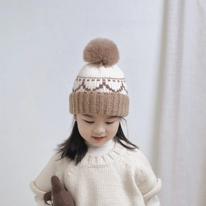 Detail of kids knit beanie with beige khaki patchwork and a large pompom on top
