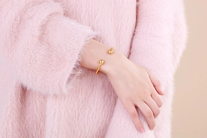 Detail of minimalist gold open bangle with dual spherical ends worn on a soft knit sleeve