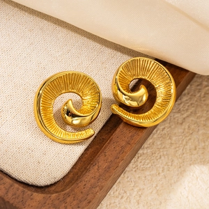 Detailed close-up of golden spiral swirl earrings with textured radial finish on linen