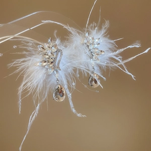 Detailed view of silver needle earrings featuring crystal teardrops and white feathers