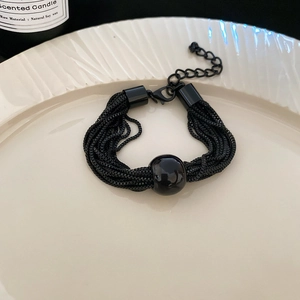 Detailed view of multilayer black chain bracelet with metal beads on a textured plate