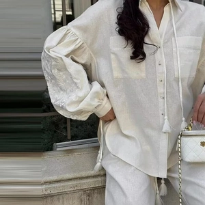 Detailed embroidery on lantern sleeves of a cream linen blend shirt with tassel ties