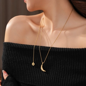 Detail of 18k gold plated croissant pendant necklace with textured finish on black knitwear