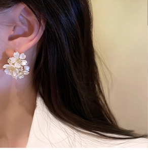 Dettaglio di orecchini a fiore crema con finiture dorate indossati da una modella