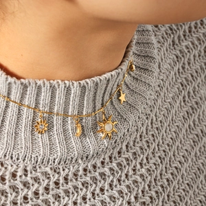 Détail du collier céleste avec pendentifs soleil lune et étoile sur un pull gris