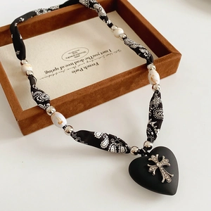 Detail of paisley fabric cord and matte black heart pendant with diamond cross charm