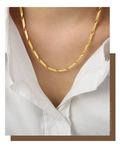 Detail shot of a gold bamboo-style necklace with Greek key pattern on a model's neck