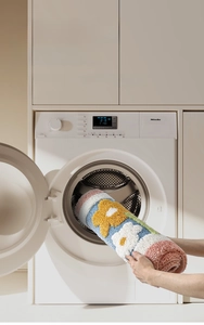 Detail of colorful floral bath mat being placed in washing machine for easy machine washing