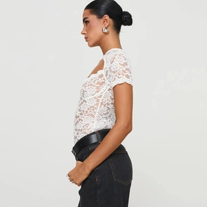 Side view of white floral lace V-neck bodysuit paired with black denim jeans and a belt
