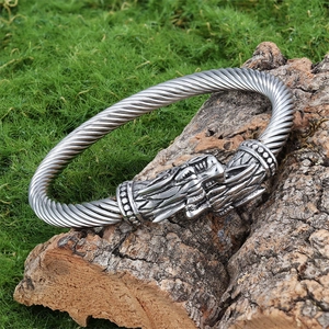Detail of silver twisted cable bracelet featuring intricately carved wolf heads on wood
