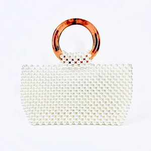 Detail of handmade pearl woven handbag featuring amber-toned round acrylic handles