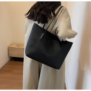 Detail of black woven texture tote bag worn on shoulder by model in minimalist setting