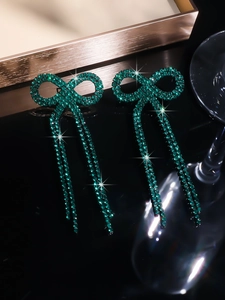 Close-up of elegant copper bow earrings with long tassels and sparkling green rhinestones