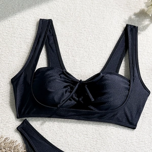 Flat lay of black bikini top with front tie bow and textured fabric on beach-themed mat