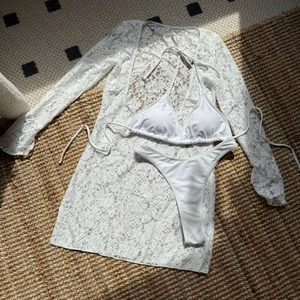 Flat lay of white three-piece lace swimwear set including long sleeve cover-up and bikini