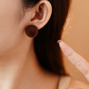 Close-up of deep brown flocked button earring with textured finish on a model's ear
