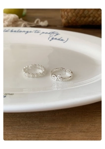 Detailed view of silver rings with hollow floral and bow designs on a ceramic plate