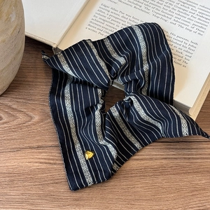 Vintage navy striped scrunchie with a gold heart charm placed on an open book
