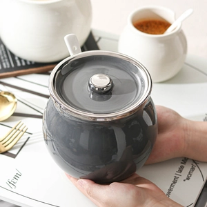 Modern grey ceramic oil jar with silver lid and ceramic spoon held in a kitchen setting