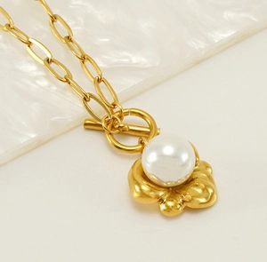 Dettaglio collana dorata con chiusura a T, pendente a fiore e perla centrale