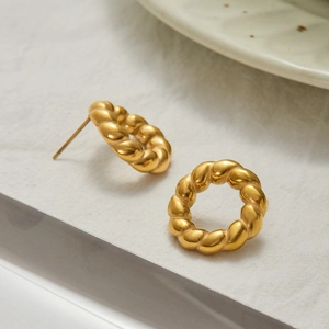 Close-up of gold-plated twisted hoop earrings with a polished finish on ceramic plate