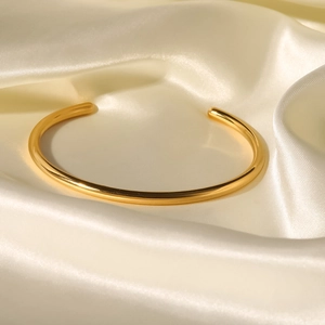 Bracciale rigido in acciaio inossidabile placcato oro 18K su sfondo di seta beige