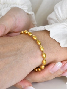 Detailed close-up of a golden oval bead chain bracelet worn on a female wrist