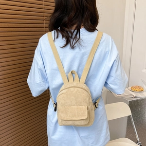 Detail view of a beige corduroy mini backpack with canvas straps worn by a model