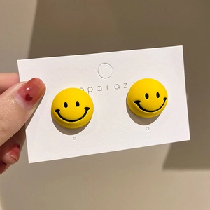 Close-up of yellow round smiley face stud earrings with matte finish and silver needle