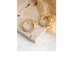 Close-up of gold-plated hoop earrings with pavé set crystals on a travertine surface