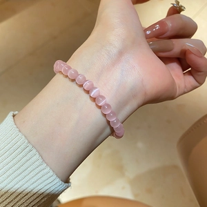 Pink cat eye stone beaded bracelet shown on wrist in a warm lifestyle setting