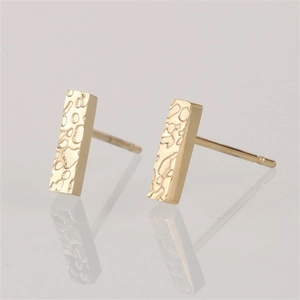 Macro detail of gold bar earrings with hammered texture on a reflective surface