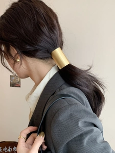 Detail of a minimalist gold metal ponytail clip showing the elegant matte brushed texture