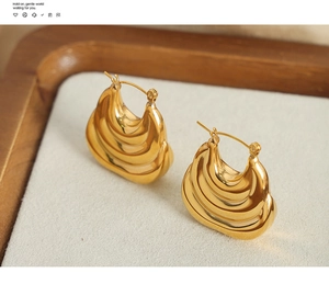 Macro shot of gold-plated wavy earrings with polished texture on beige velvet padding