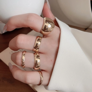 Close-up of five varied width gold geometric rings worn by a model on a neutral background