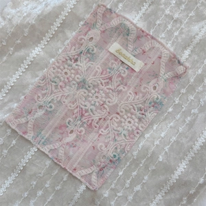 Detailed view of pink floral lace fabric with white embroidery and Sesame woven label