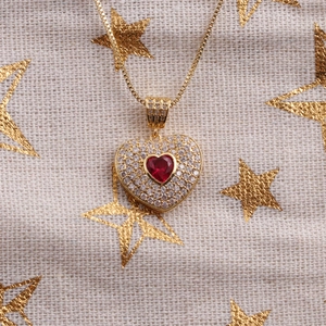 Détail d'un collier cœur doré avec pierre précieuse rouge et accents de zircone clair