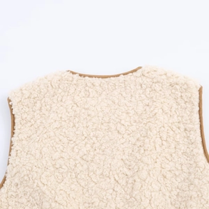 Close-up of cream faux shearling vest featuring brown trim and textured fleece fabric