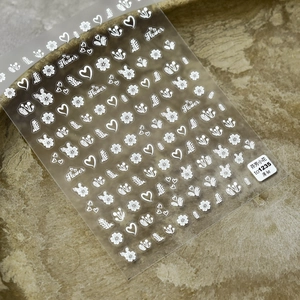 Dettaglio di adesivi per nail art con fiori bianchi e foglie su sfondo di pietra